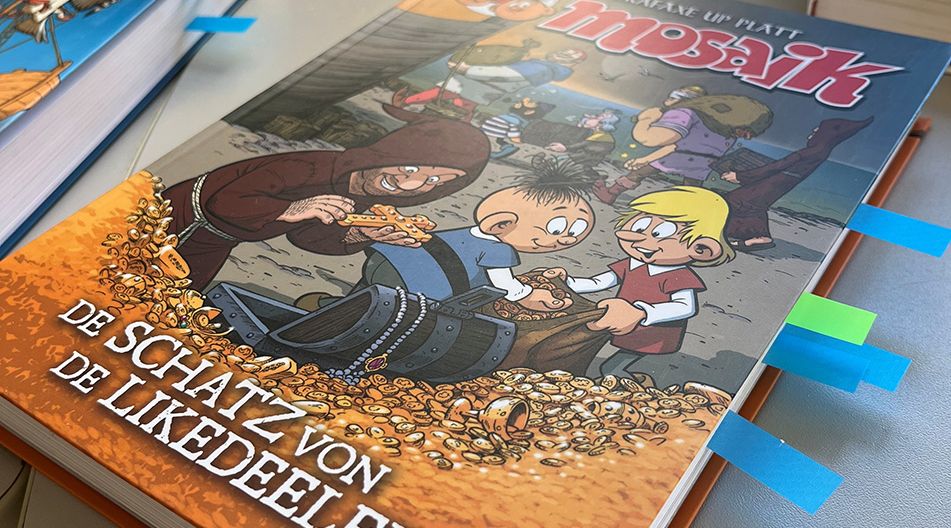 Kinderbuch „Mosaik – De Schatz von de Likedeele“ mit Comicfiguren und Schatzkiste voller Goldmünzen auf dem Cover.