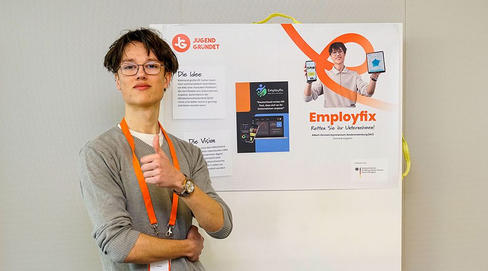 Eine Person mit Brille und orangefarbenem Band zeigt Daumen hoch vor einem Präsentationsposter mit dem Titel „Employfix“.